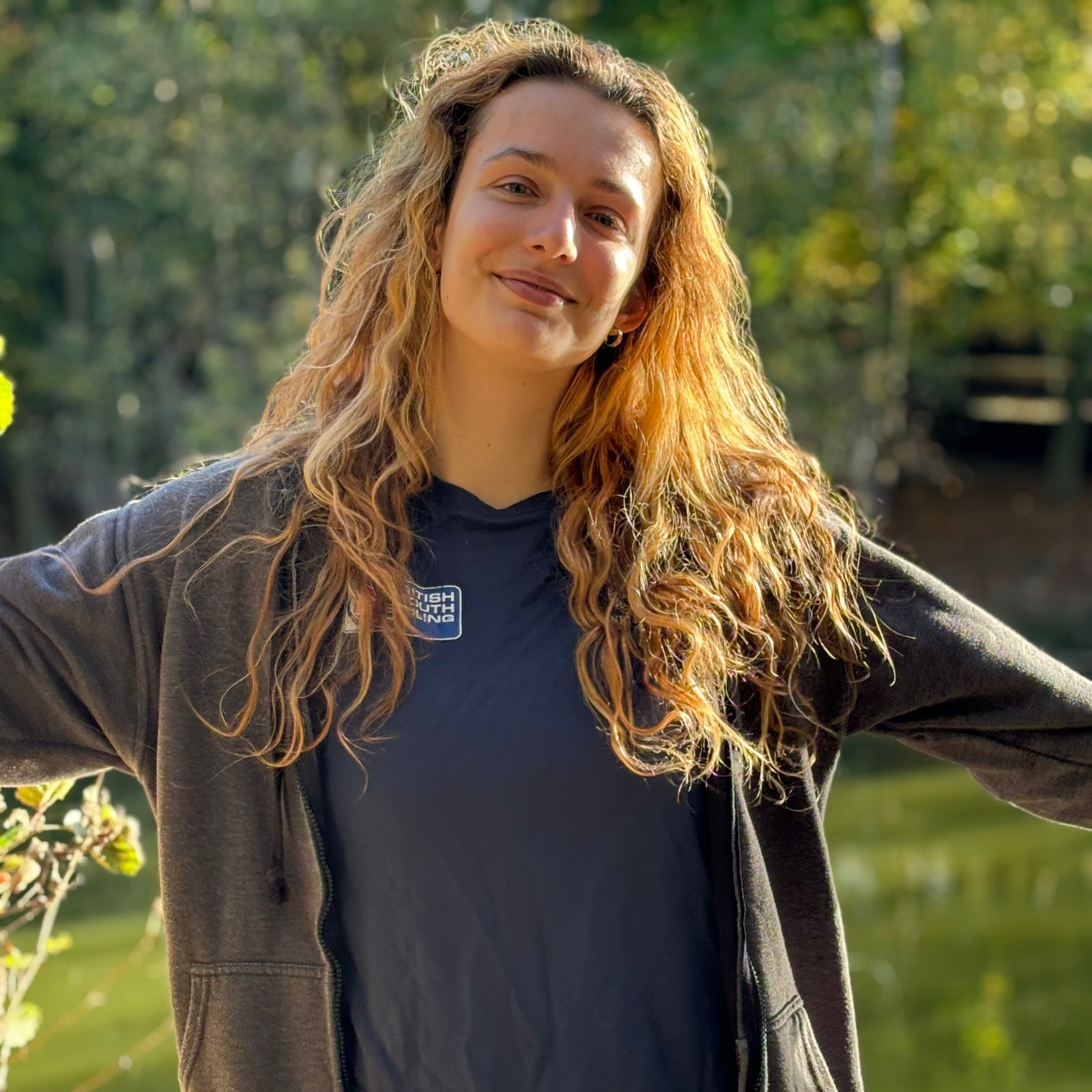 A female-presenting indivual with blonde hair smiling for a photo in an outdoor space
