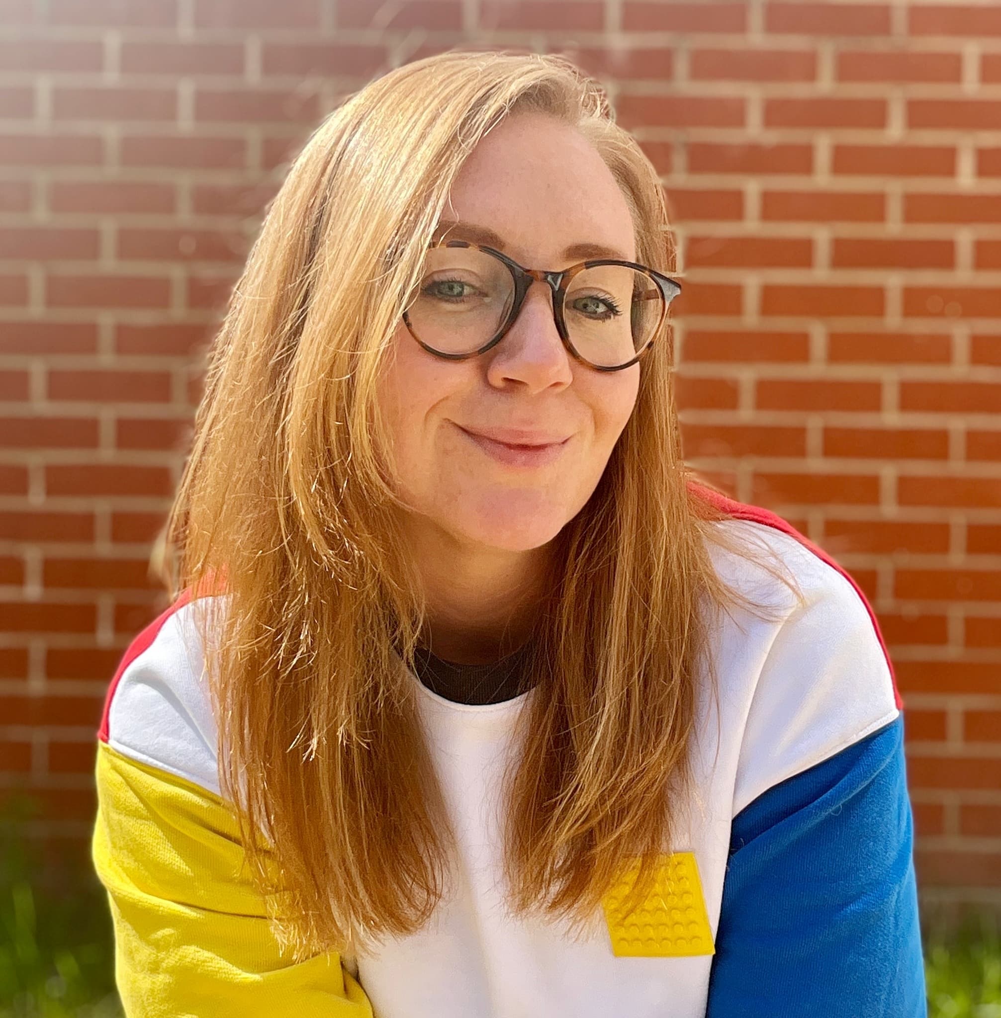 A portrait of a female-appearing person with blonde hair and glasses